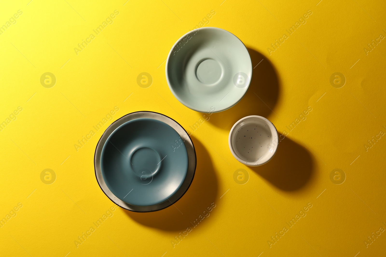 Photo of Clean ceramic plates and bowl on yellow background, flat lay
