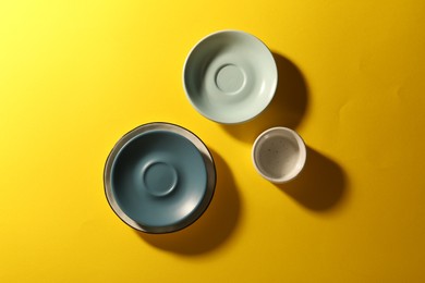 Clean ceramic plates and bowl on yellow background, flat lay