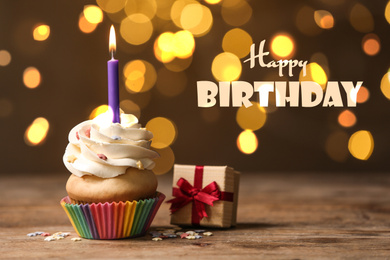 Delicious cupcake and gift box on wooden table against blurred lights. Happy Birthday