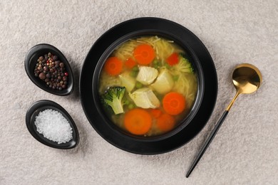 Photo of Tasty chicken soup with noodles and vegetables in bowl served on light textured table, flat lay