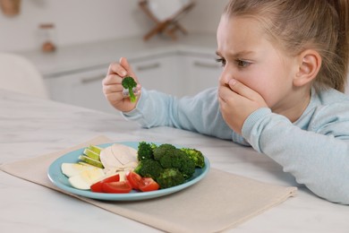 Photo of Cute little girl covering mouth and refusing to eat dinner in kitchen