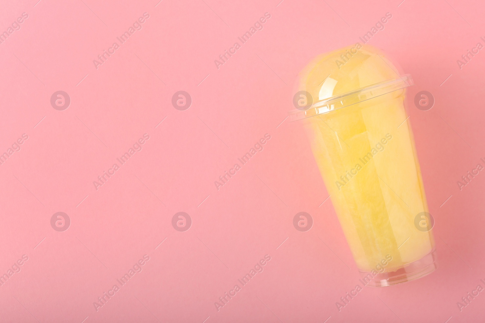 Photo of Sweet cotton candy in plastic cup on pink background, top view. Space for text