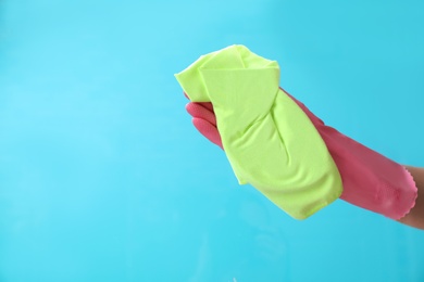 Photo of Woman cleaning glass with rag against color background