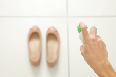 Photo of Woman spraying deodorant over pair of shoes at home, closeup. Space for text