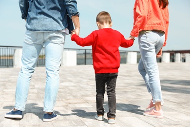 Photo of Little child holding hands with his parents outdoors. Family weekend