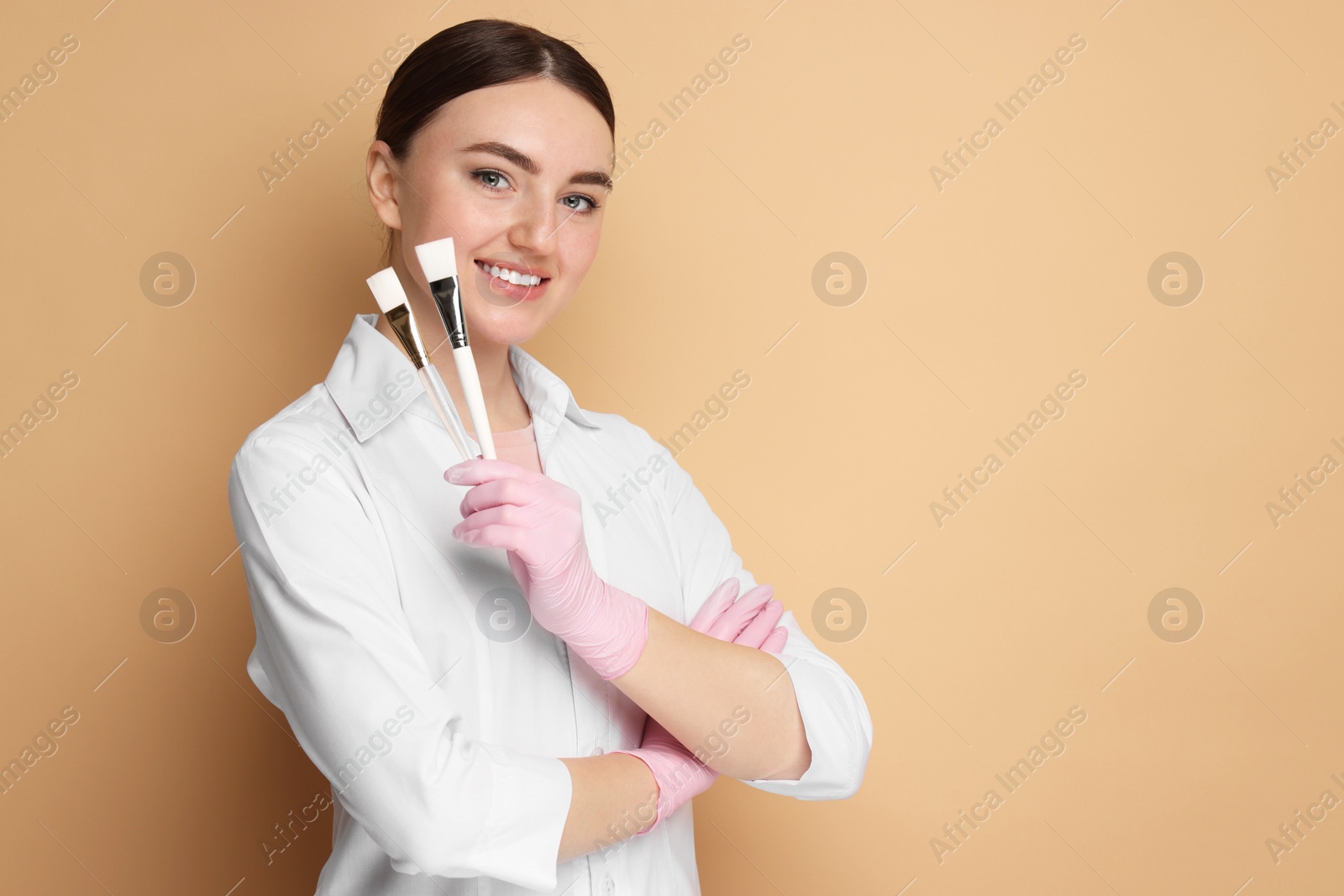 Photo of Cosmetologist with cosmetic brushes on beige background, space for text