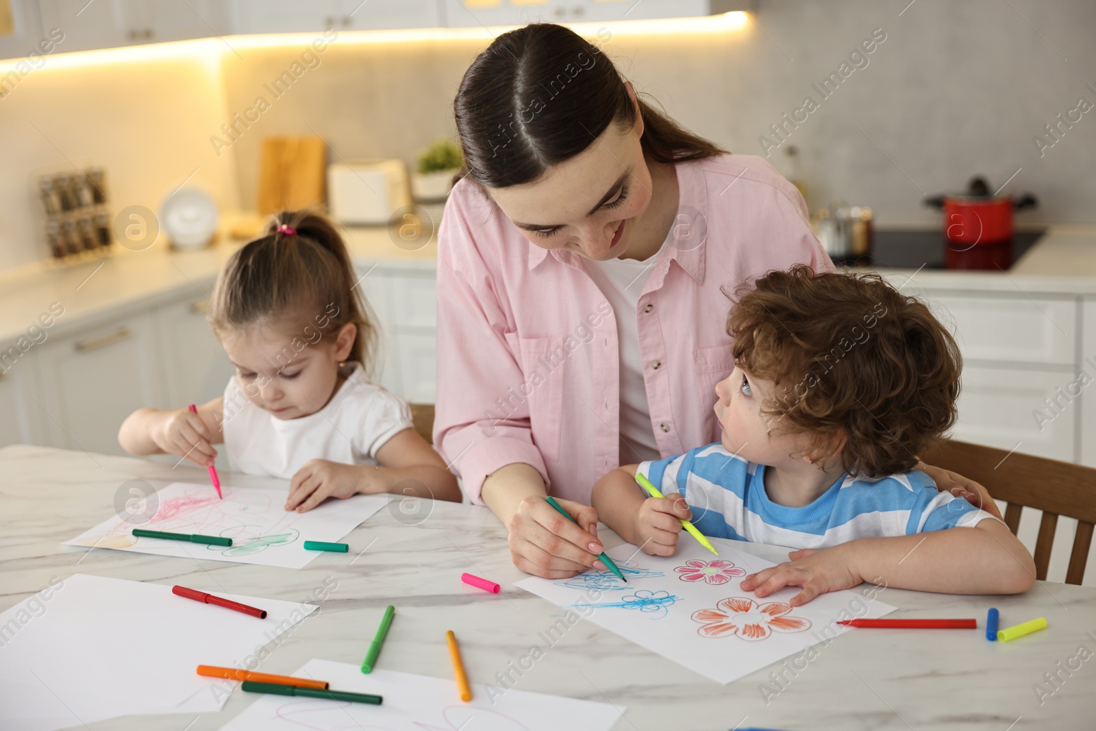 Photo of Mother and her little children drawing with colorful markers at table in kitchen