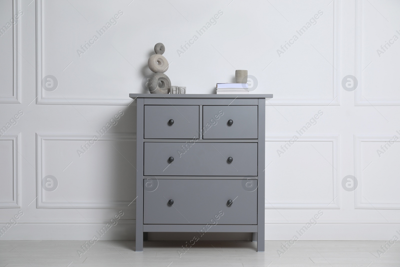 Photo of Different accessories on grey chest of drawers near white wall indoors