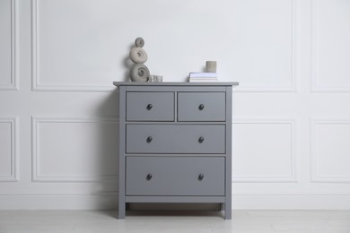 Photo of Different accessories on grey chest of drawers near white wall indoors