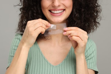 Photo of Young woman holding teeth whitening strips on grey background, closeup