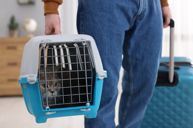 Travel with pet. Man holding carrier with cute cat and suitcase at home, closeup