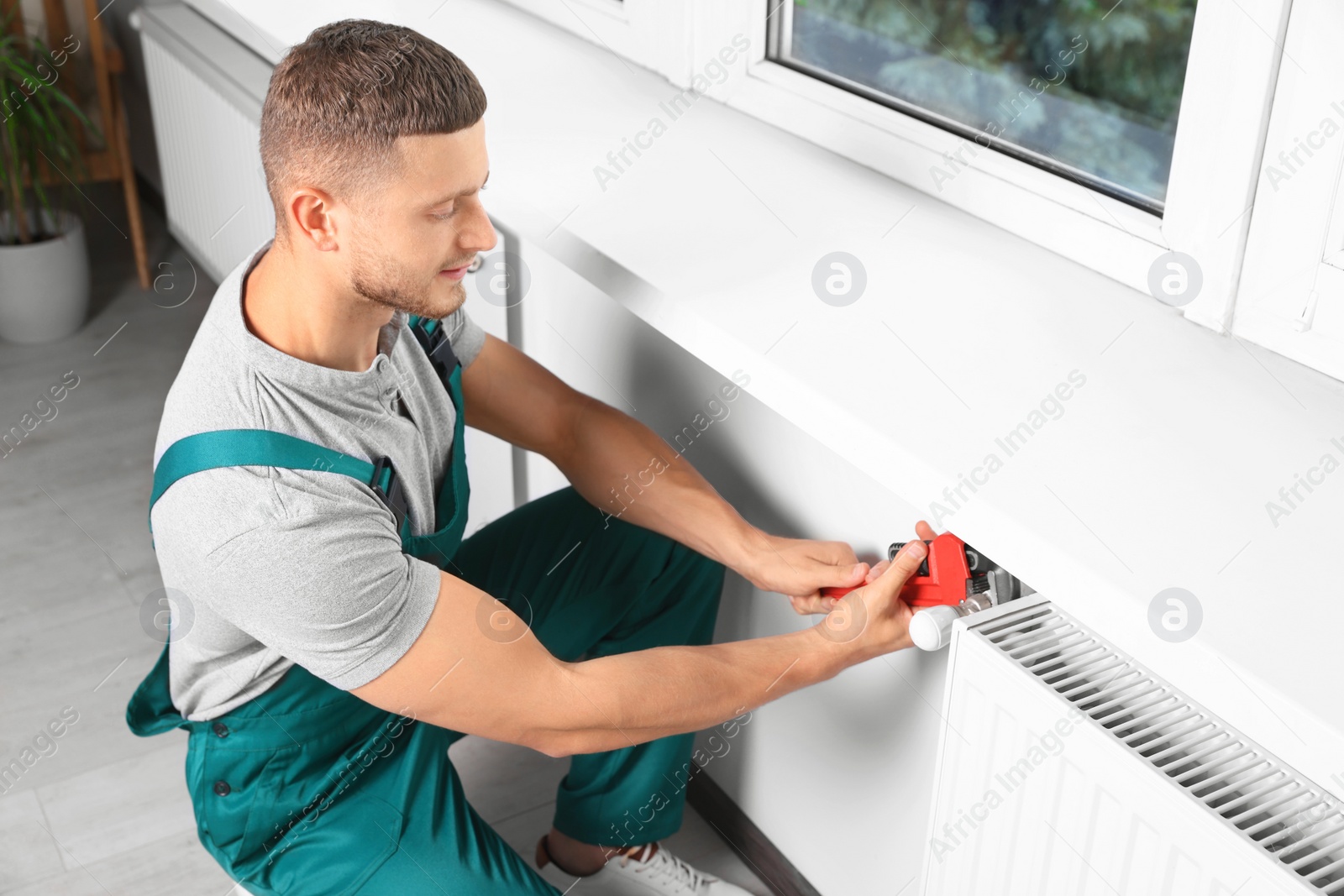 Photo of Professional plumber using adjustable wrench for installing new heating radiator in room