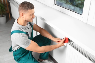 Professional plumber using adjustable wrench for installing new heating radiator in room