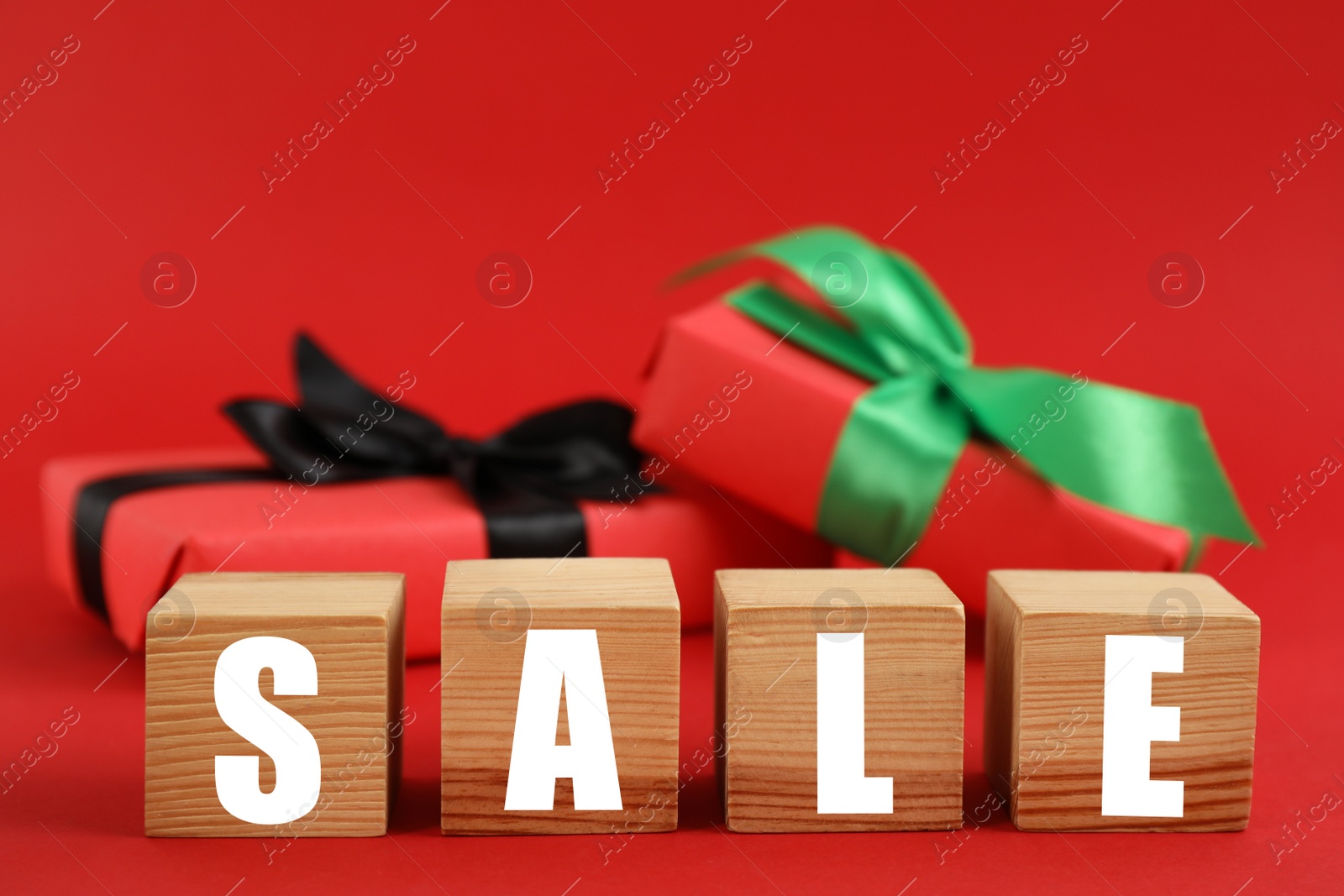 Photo of Word Sale made with wooden cubes and gift boxes on red background