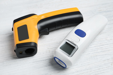 Photo of Modern non-contact infrared thermometers on white wooden background