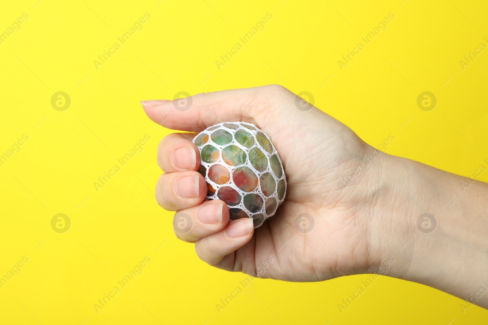 Photo of Woman holding colorful slime on yellow background, closeup. Antistress toy