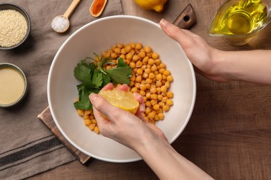 Photo of Woman squeezing lemon juice onto chickpeas at wooden table, top view. Cooking delicious hummus