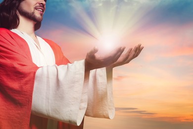 Image of Jesus Christ reaching out his hands and praying at sunset