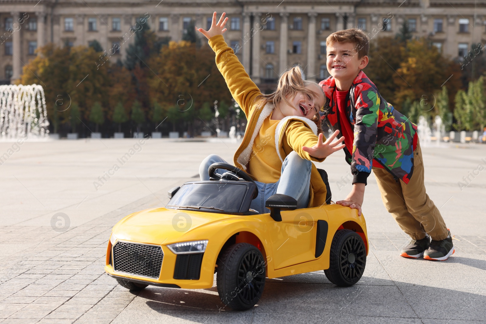 Photo of Cute boy pushing children's car with little girl outdoors on sunny day