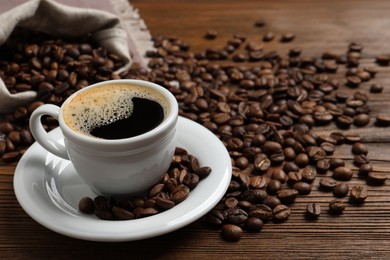 Cup of aromatic hot coffee and beans on wooden table, space for text