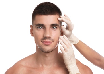 Photo of Doctor examining man's face for cosmetic surgery on white background