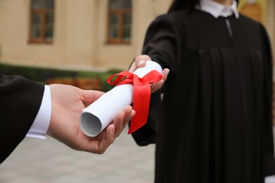 Photo of Student receiving diploma during graduation ceremony outdoors, closeup
