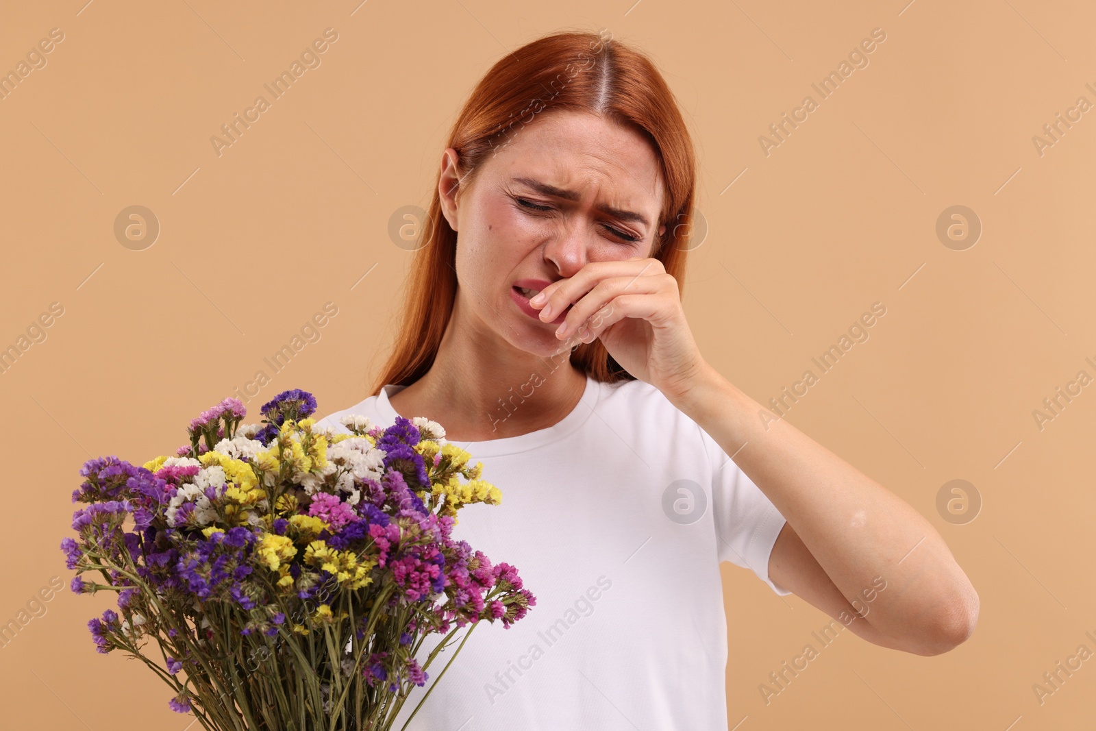 Photo of Suffering from allergy. Young woman with flowers sneezing on beige background