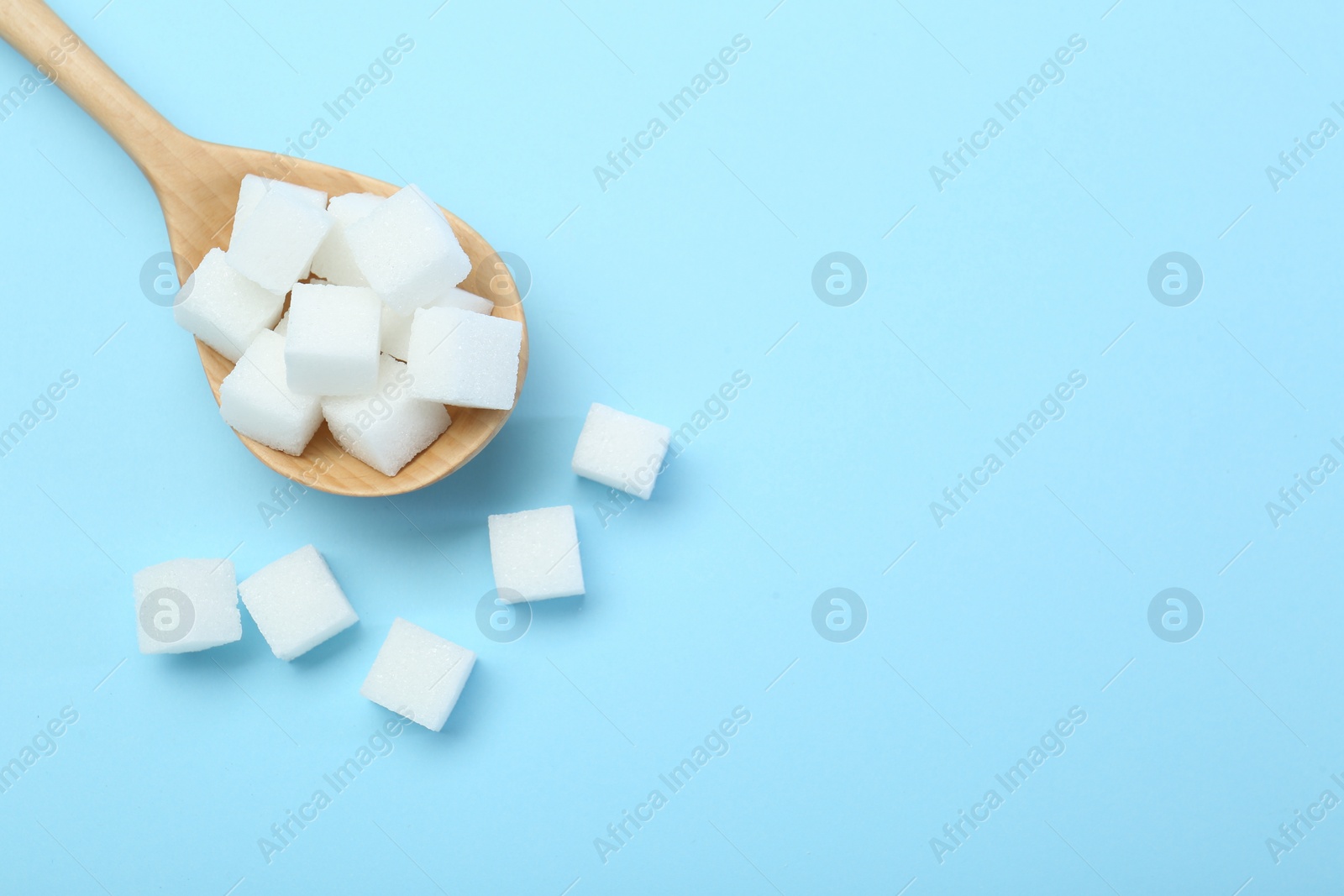 Photo of White sugar cubes and wooden spoon on light blue background, top view. Space for text