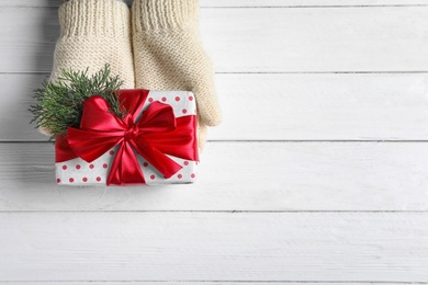 Woman wearing mittens holding Christmas gift on wooden background, top view