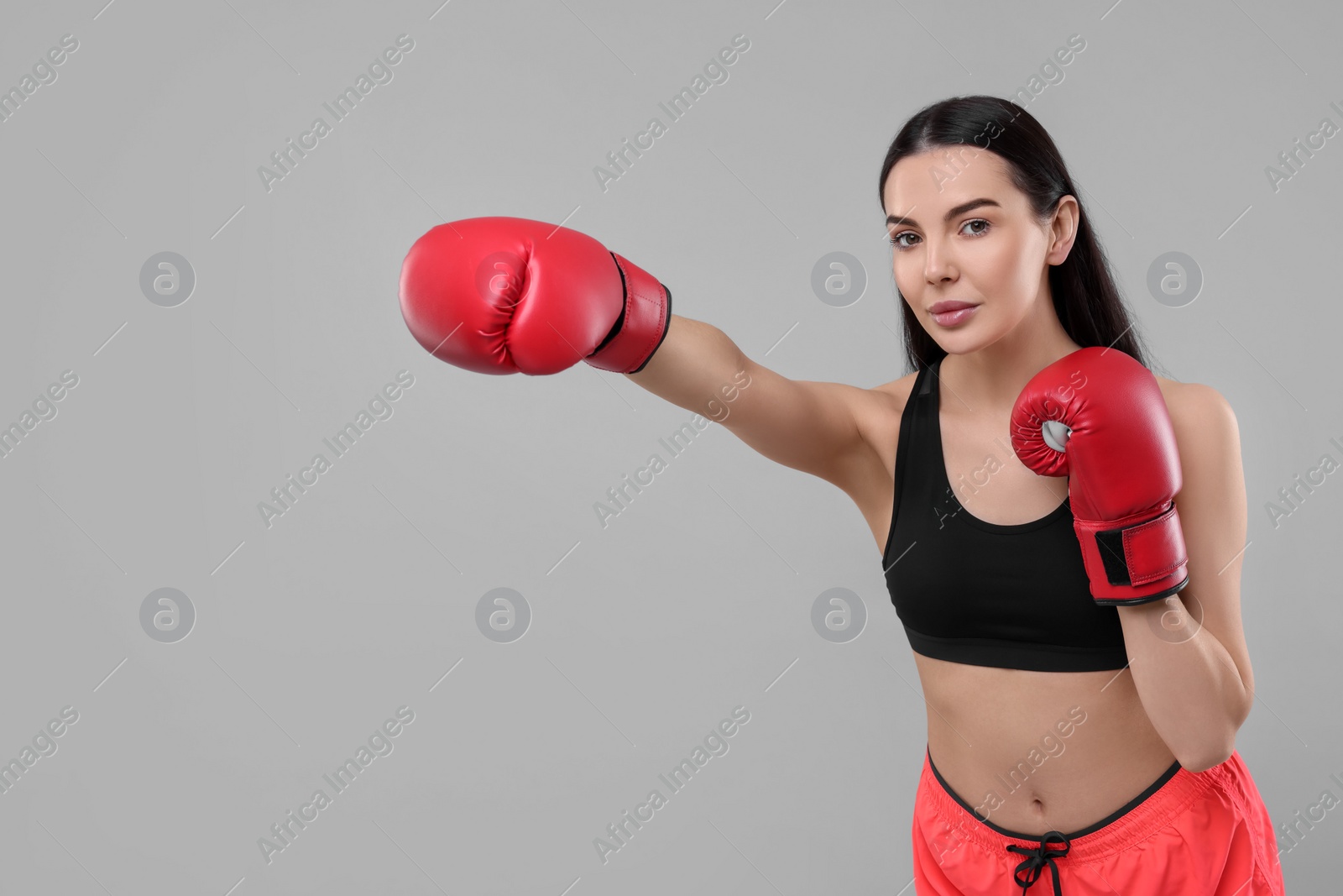 Photo of Beautiful woman in boxing gloves training on grey background. Space for text