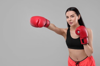 Beautiful woman in boxing gloves training on grey background. Space for text