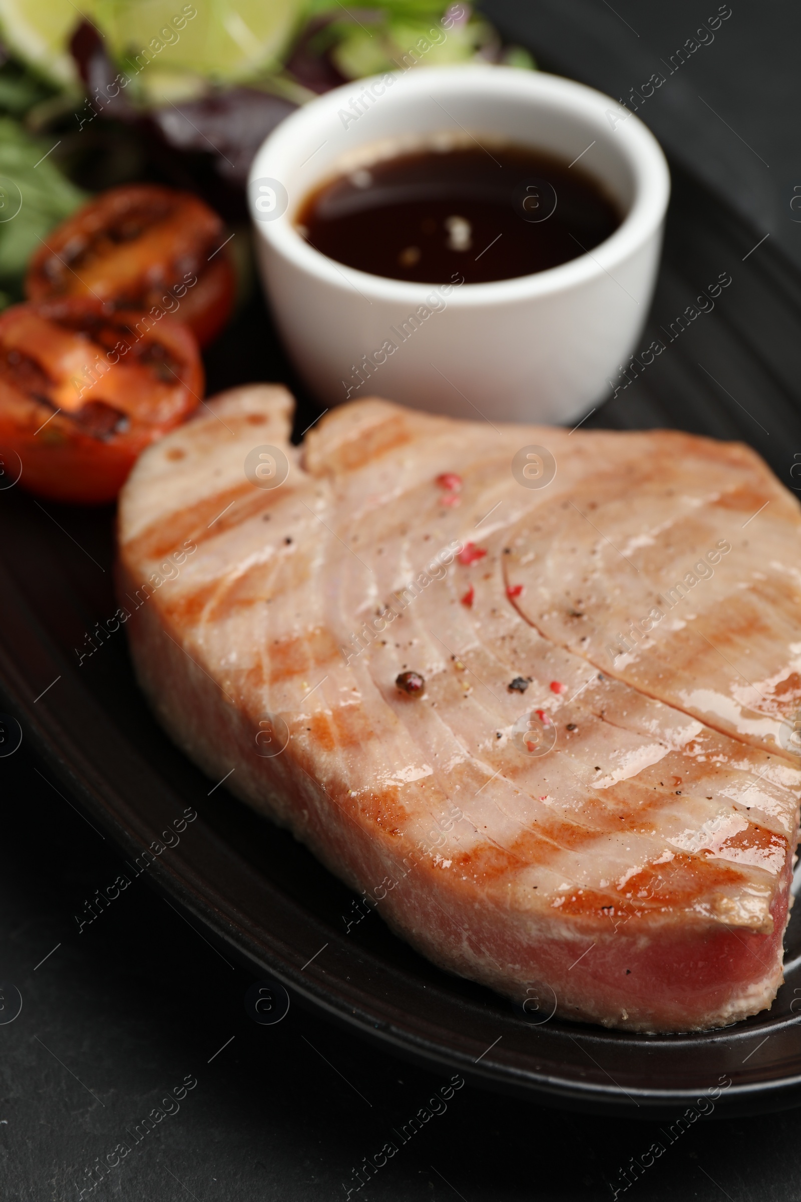 Photo of Delicious tuna steak, tomato and sauce on black table, closeup