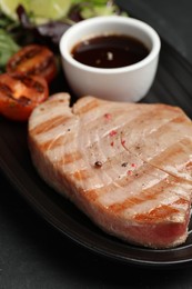 Delicious tuna steak, tomato and sauce on black table, closeup