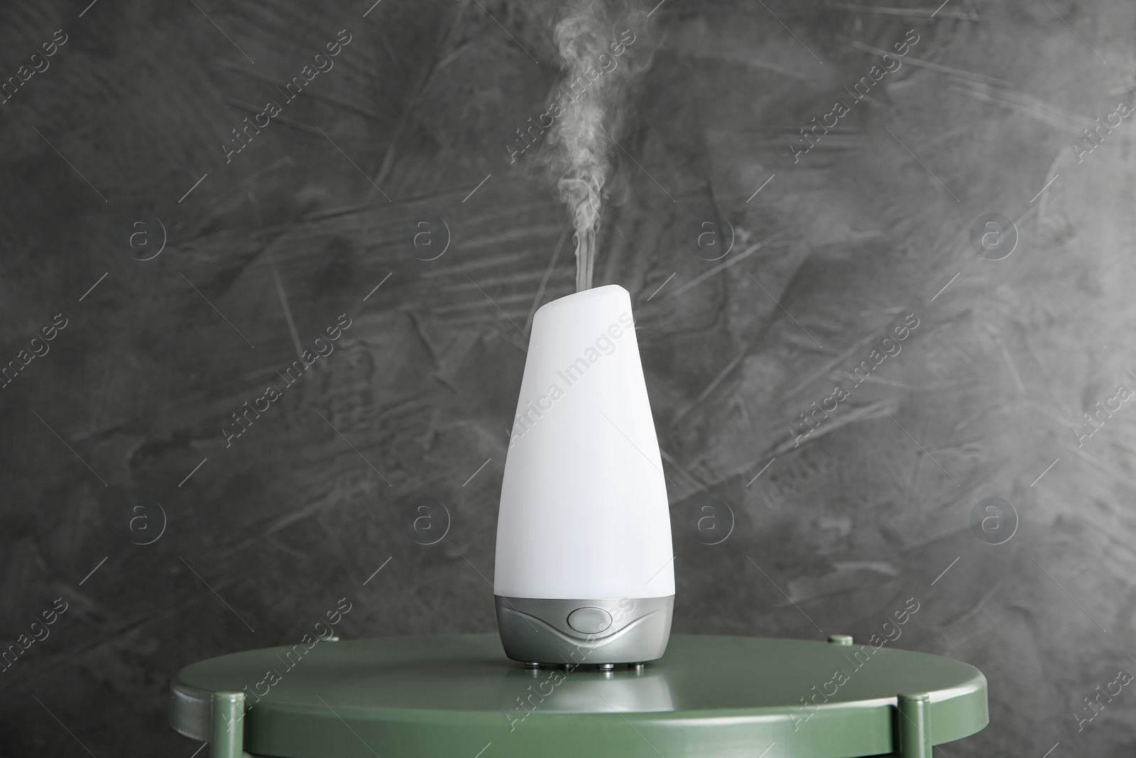 Photo of Modern essential oil diffuser on green table against dark grey background