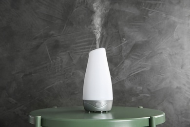 Photo of Modern essential oil diffuser on green table against dark grey background