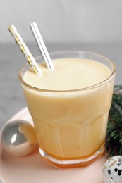 Photo of Glass of delicious eggnog and decorated fir branch on gray table, closeup