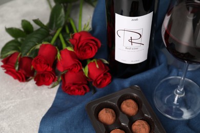 Red wine, chocolate truffles and roses on light textured table, closeup