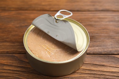 Open tin can with meat pate on wooden table, closeup