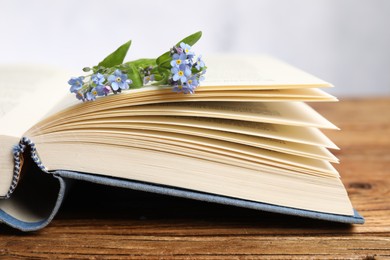 Beautiful forget-me-not flowers and book on wooden table against light background, closeup