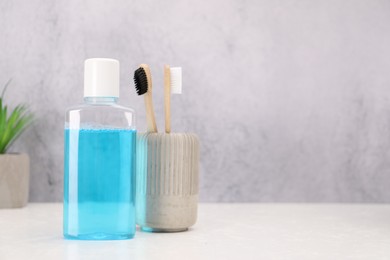 Bottle of mouthwash and toothbrushes on white table in bathroom, space for text