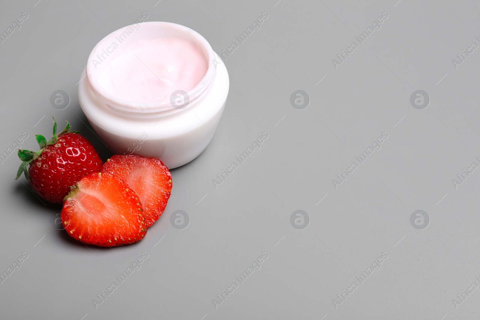 Photo of Jar of body cream and strawberries on grey background. Space for text