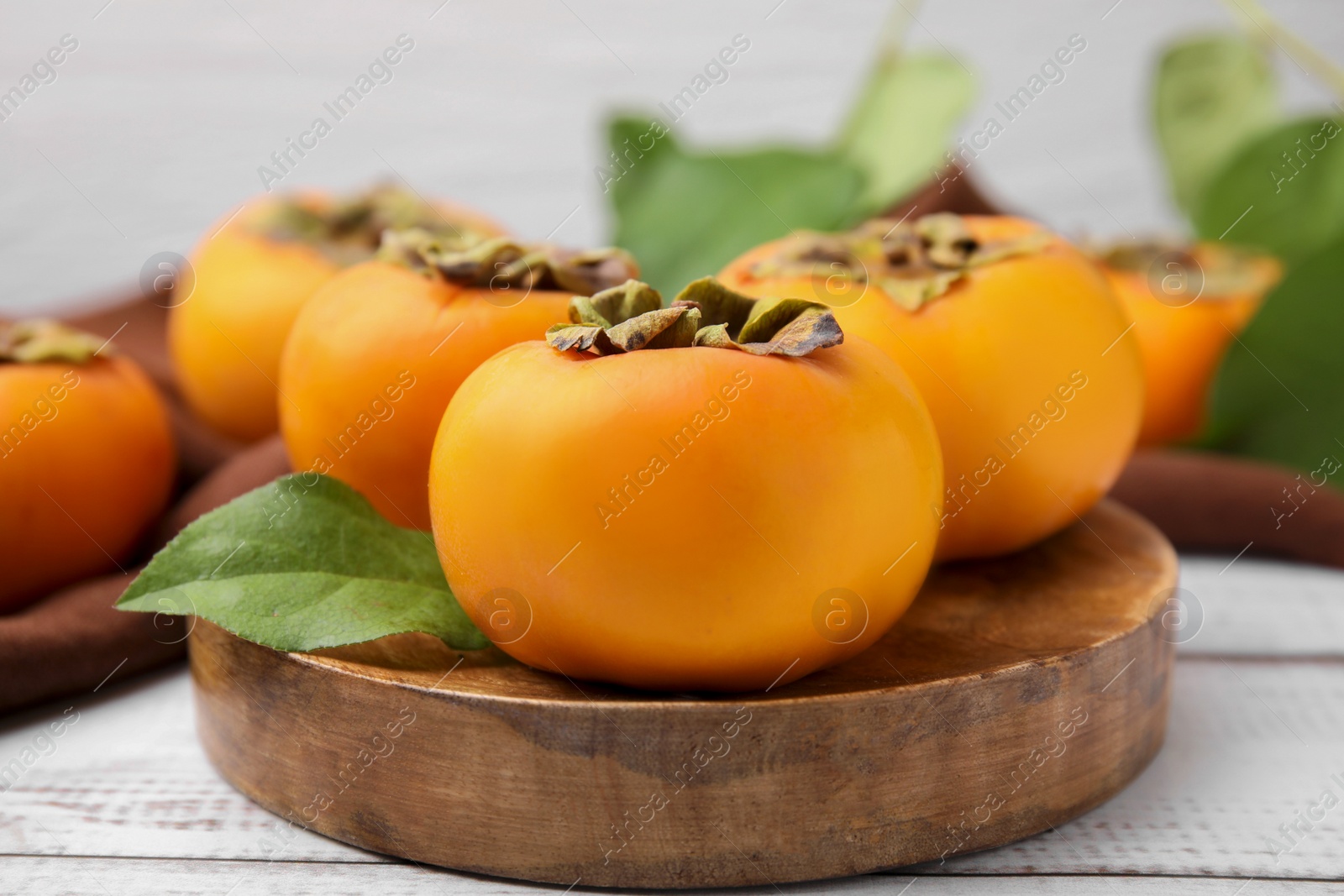 Photo of Delicious ripe juicy persimmons on white wooden table, closeup