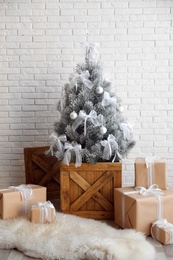 Stylish room interior with beautiful Christmas tree and gifts near white brick wall