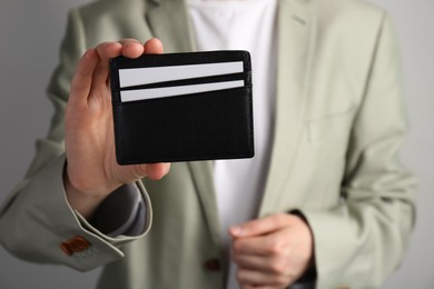 Woman holding leather business card holder with cards on grey background, closeup