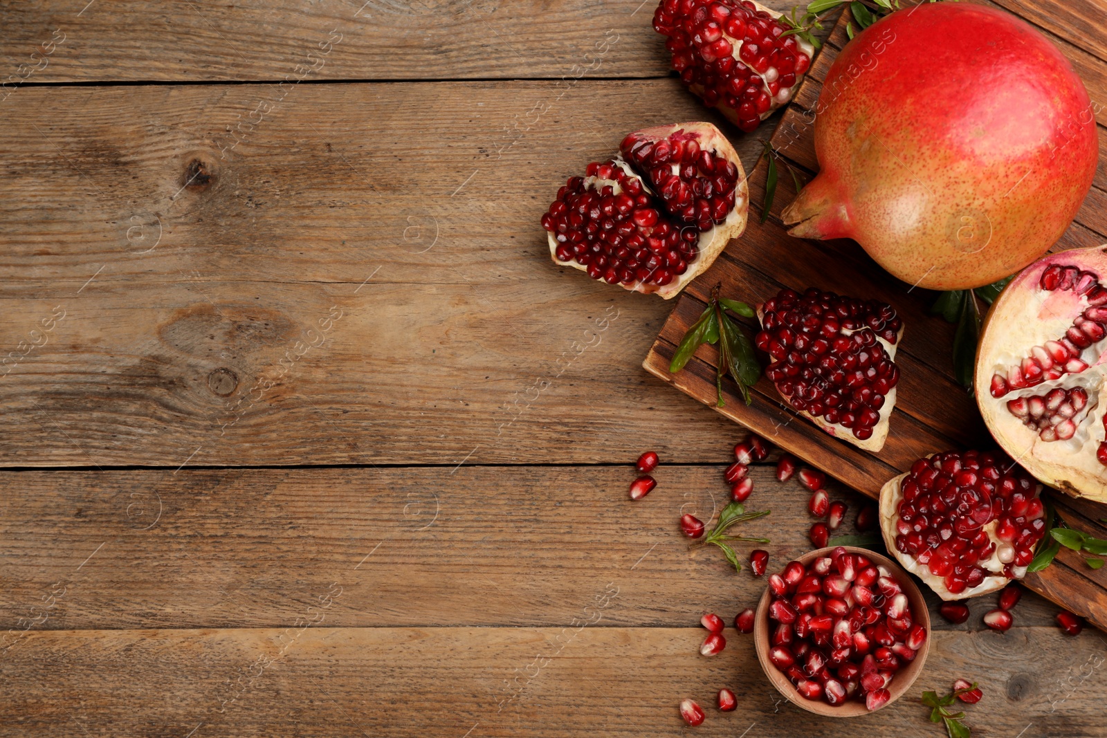 Photo of Delicious ripe pomegranates on wooden table, flat lay. Space for text