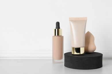 Photo of Makeup sponge, bottle and tube of skin foundation near white wall, space for text