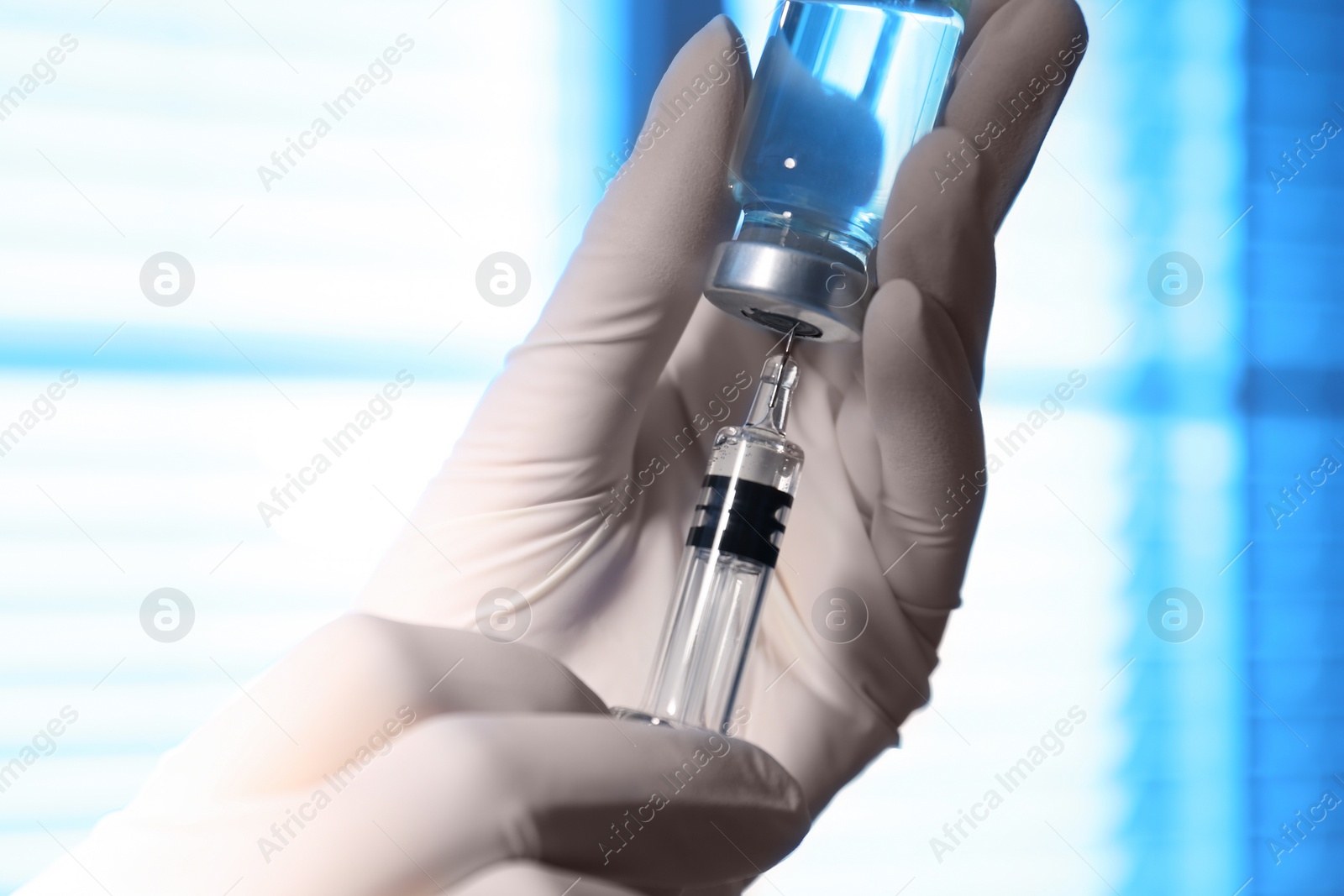 Photo of Woman filling syringe with vaccine from vial on blurred background, closeup