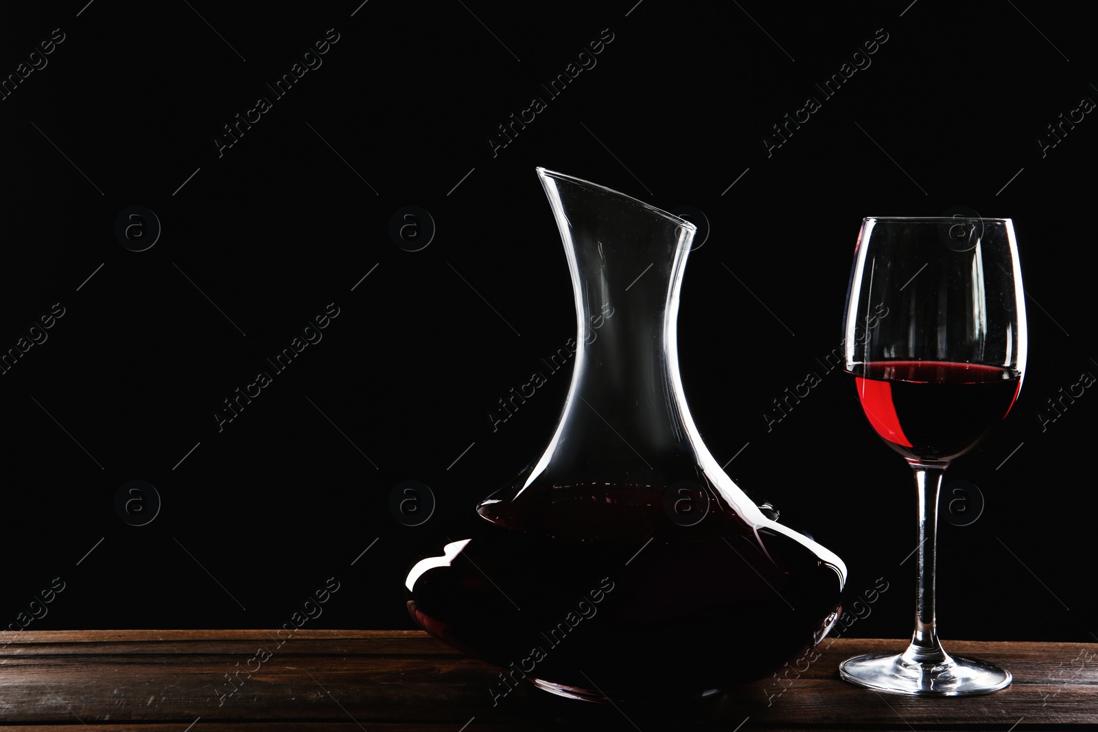 Photo of Elegant decanter and glass with red wine on table against dark background