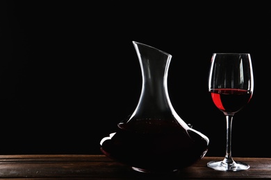 Photo of Elegant decanter and glass with red wine on table against dark background