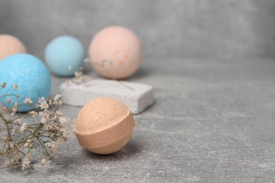 Beautiful aromatic bath bombs and gypsophila flowers on light grey table, space for text